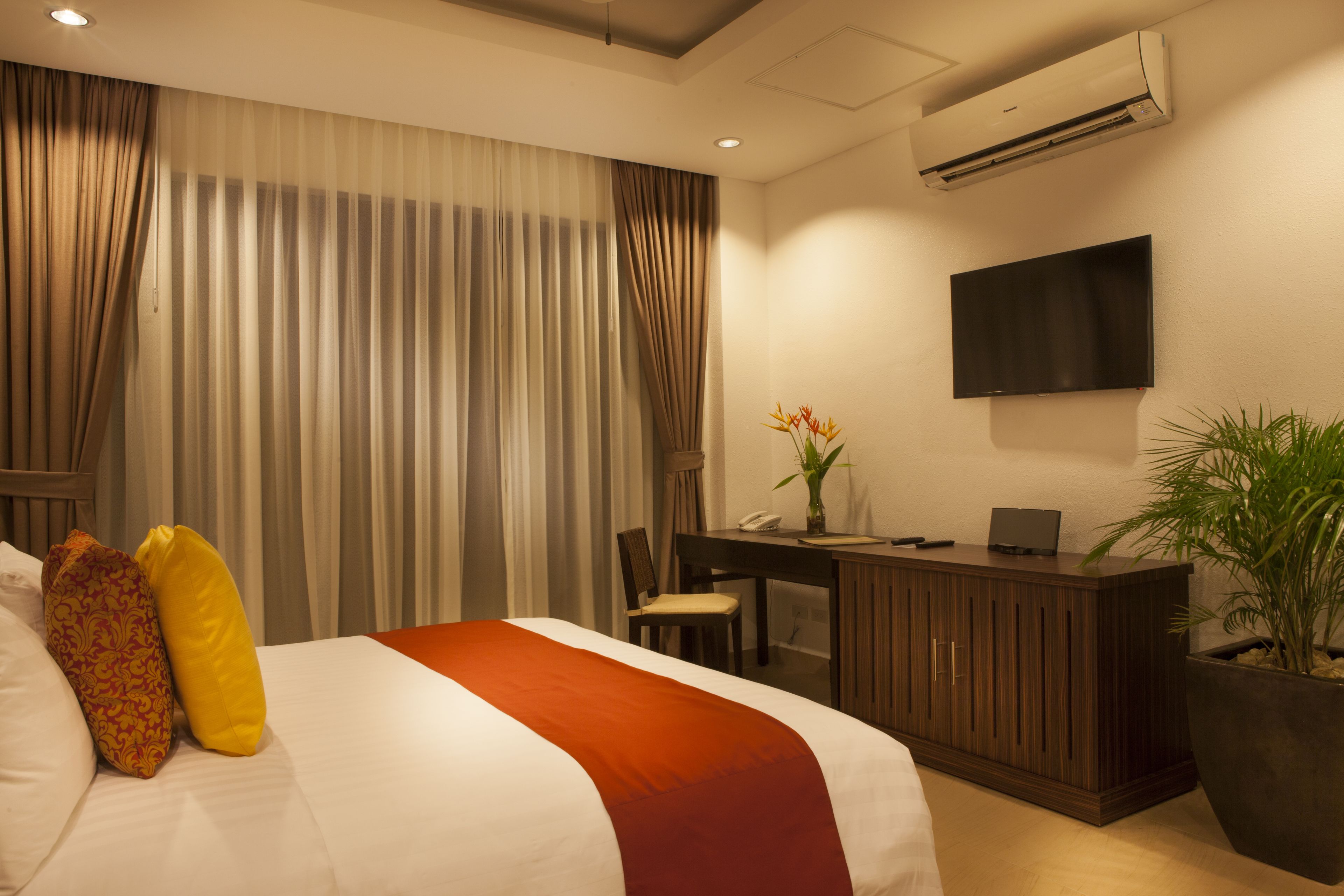 Una habitación de hotel con una cama, un escritorio, una silla, un televisor y una planta en maceta.