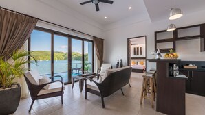 A modern living room with a large window, a ceiling fan, and a bar area. - Busuanga Bay Lodge (Busuanga)