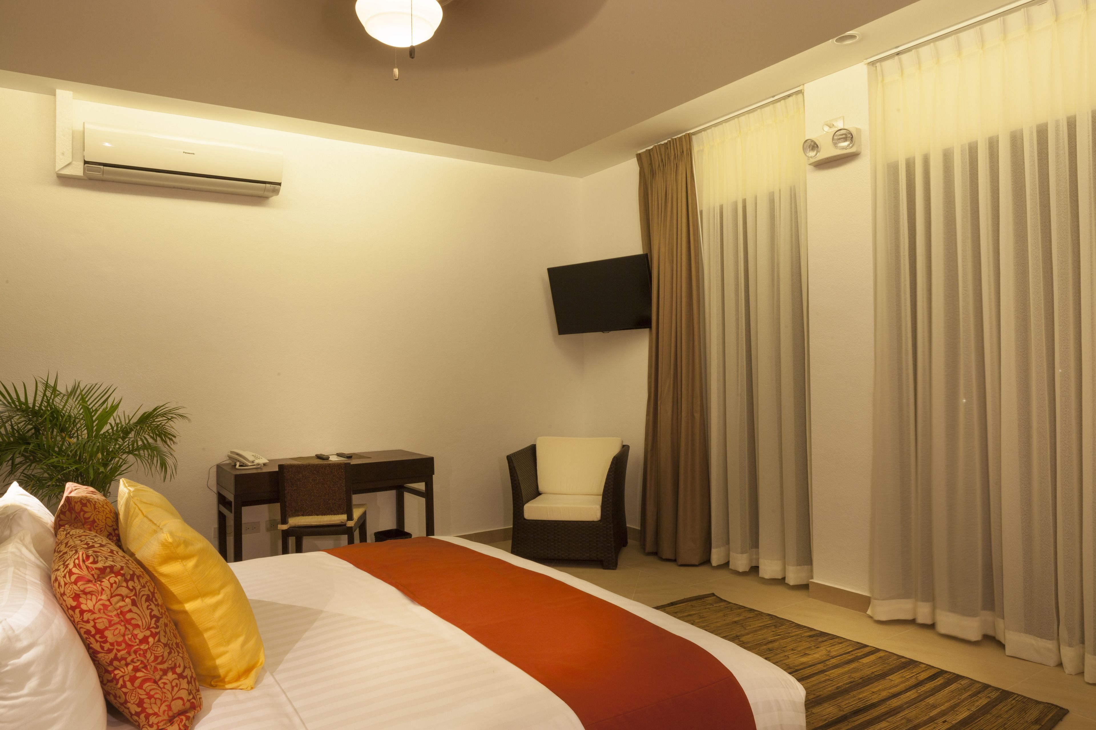 Una habitación de hotel con cama, escritorio, silla, televisor y cortinas.