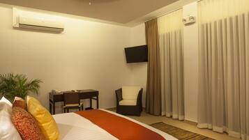 Una habitación de hotel con cama, escritorio, silla, televisor y cortinas.
