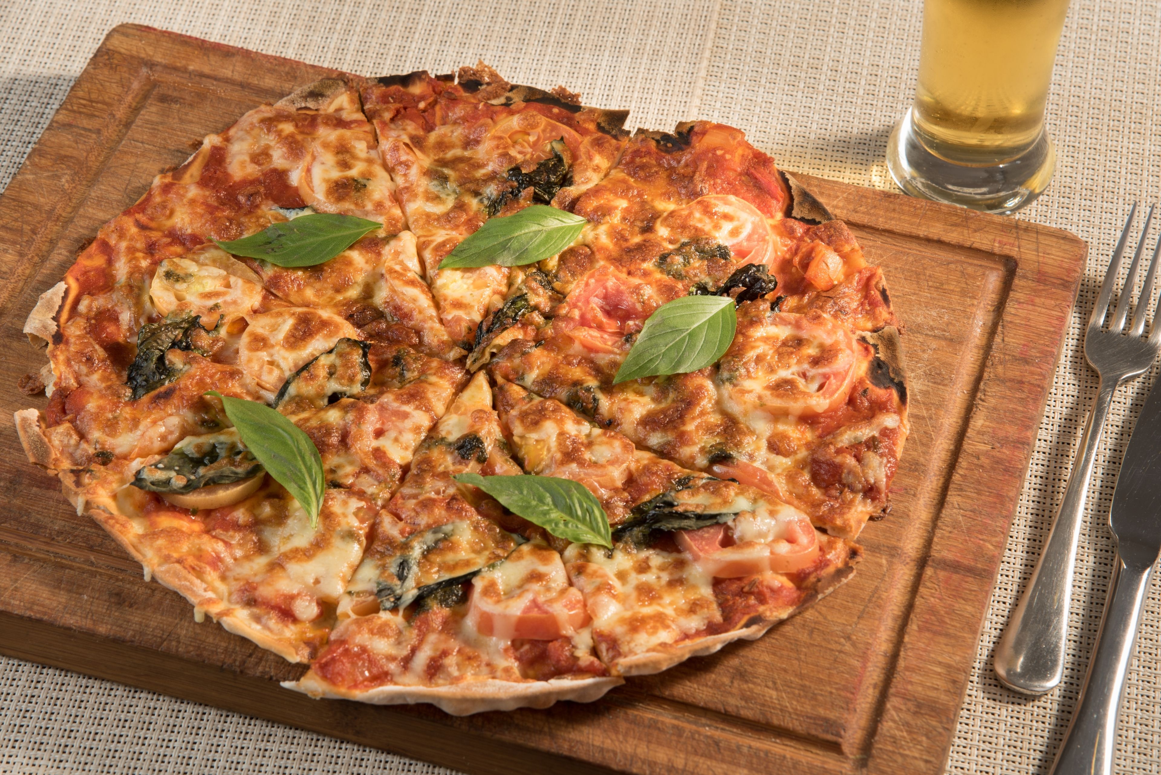 Une pizza servie sur une planche en bois, avec une fourchette et un couteau à côté.