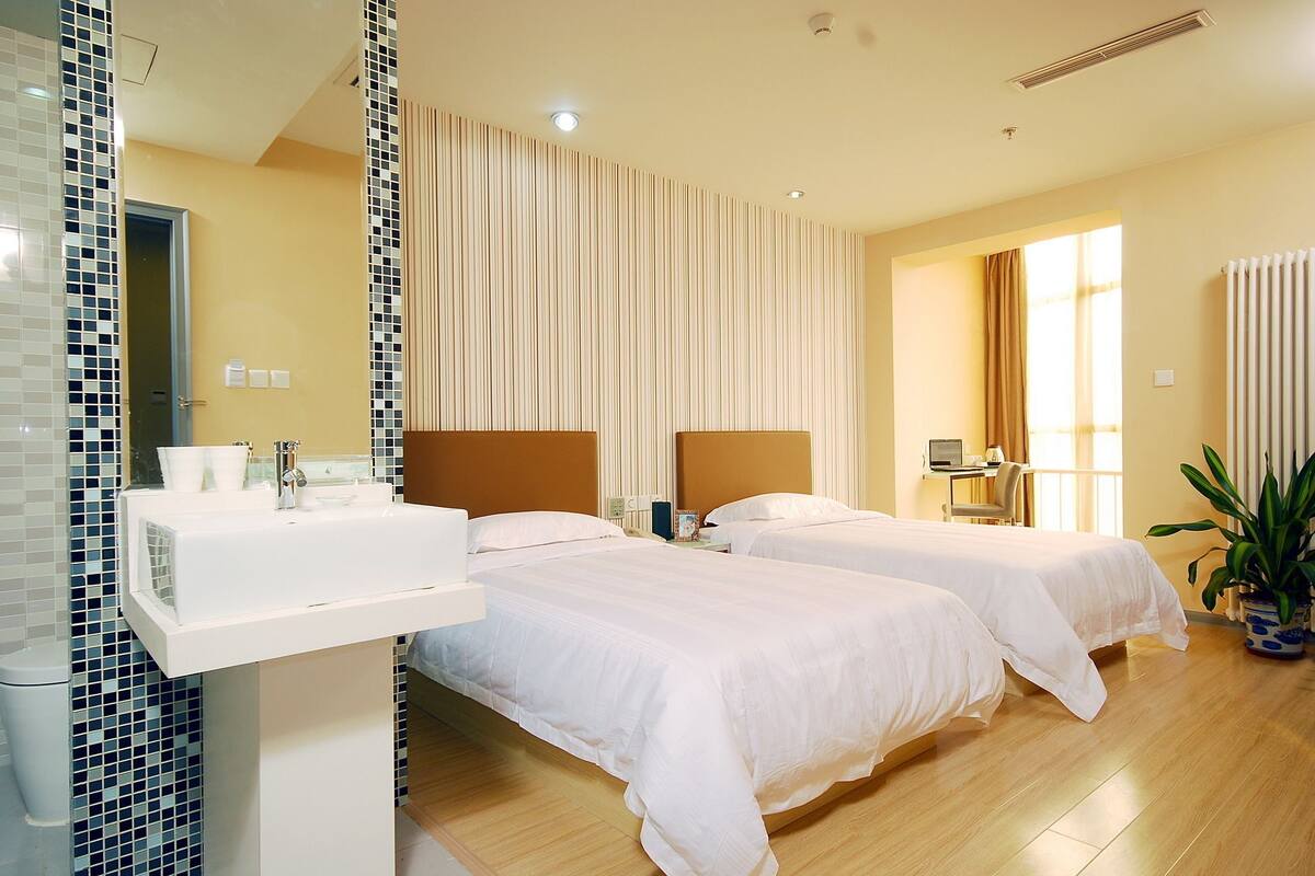 A hotel room with two beds, a bathroom with a sink, and a large window with curtains.