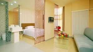 A modern hotel room with a bed, a glass coffee table with flowers, a sofa, a bathroom with a sink and mirror, and a decorative wall panel. - Shanshui Trends Hotel Liu Li Qiao (Beijing)