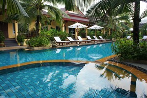 A swimming pool with tiled edges, lounge chairs, umbrellas, and tropical plants.
