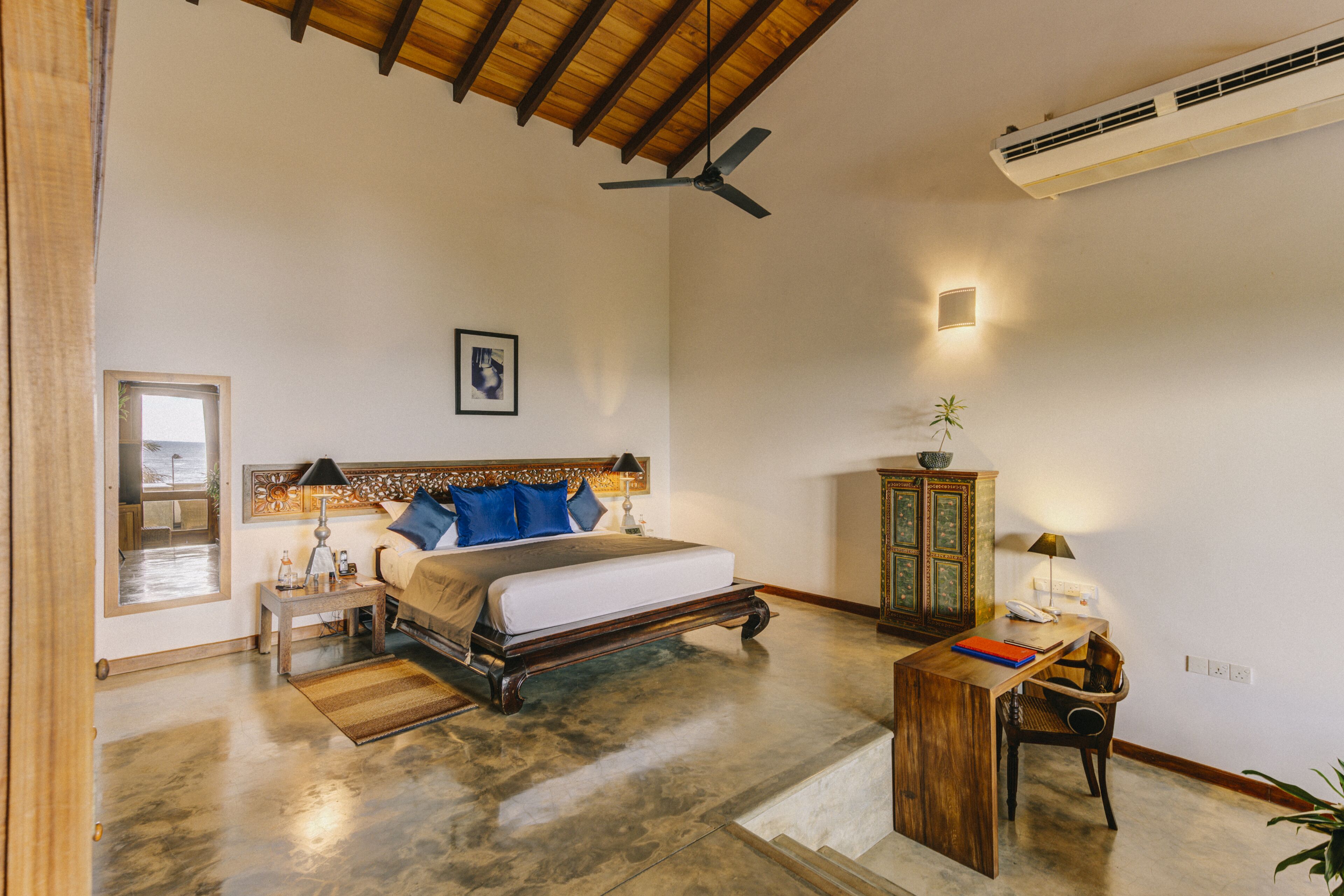 A bedroom with a bed, bedside table, lamp, and a desk with chair.