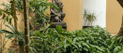 A courtyard with a stone statue, bamboo plants, and a potted plant.