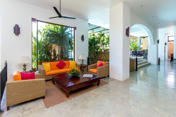 A spacious living area with wicker furniture, a coffee table, and a view of lush greenery outside. - Aditya Boutique Hotel (Hikkaduwa)
