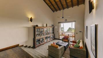 A spacious living area with a high ceiling, a large bookshelf, comfortable seating, and a view through a glass door.