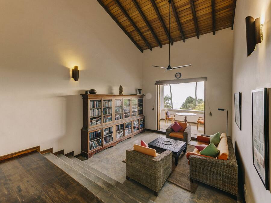 A spacious living area with a high ceiling, a large bookshelf, comfortable seating, and a view through a glass door.