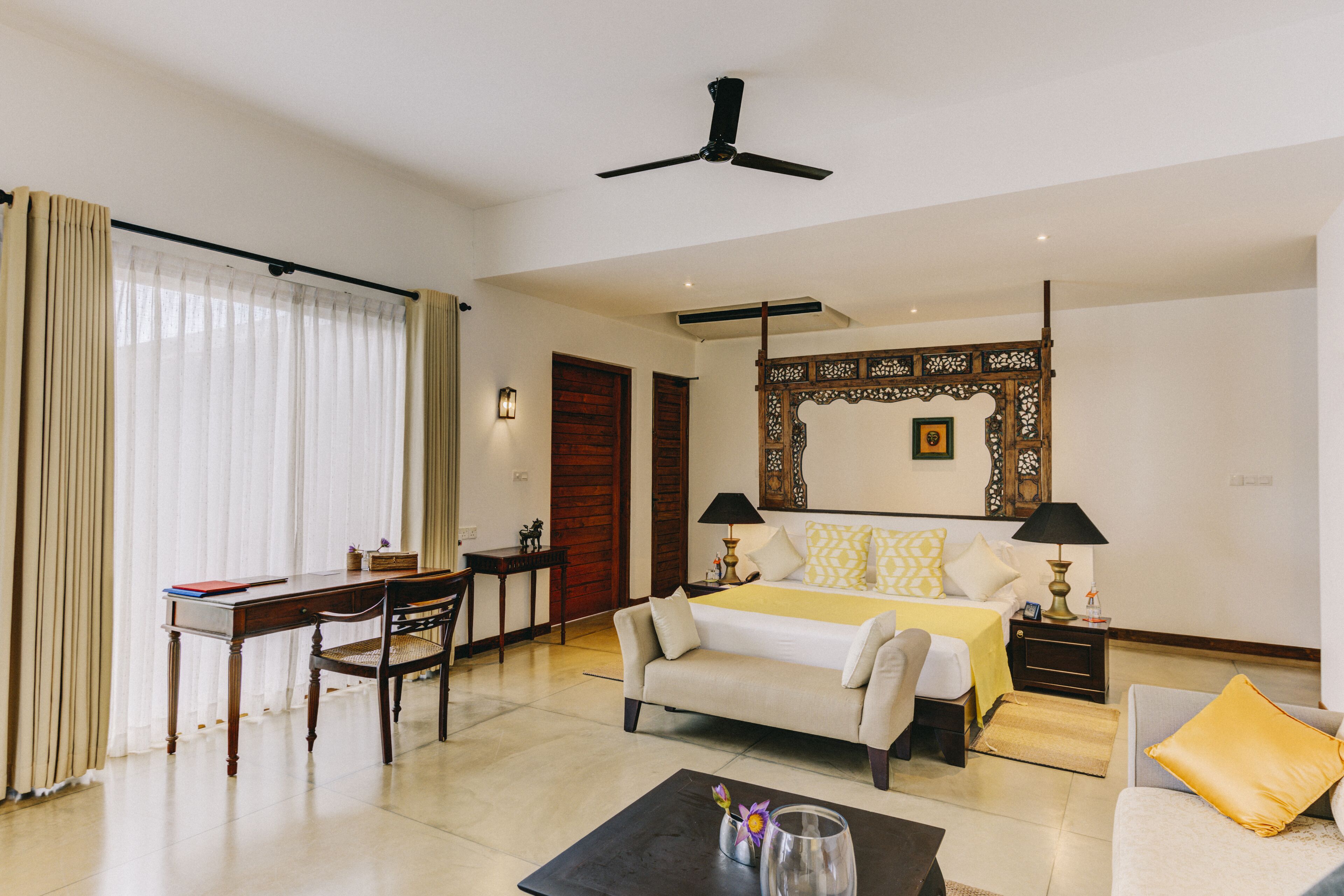 Una habitación de hotel con cama, escritorio, silla, mesa de centro y ventilador de techo.