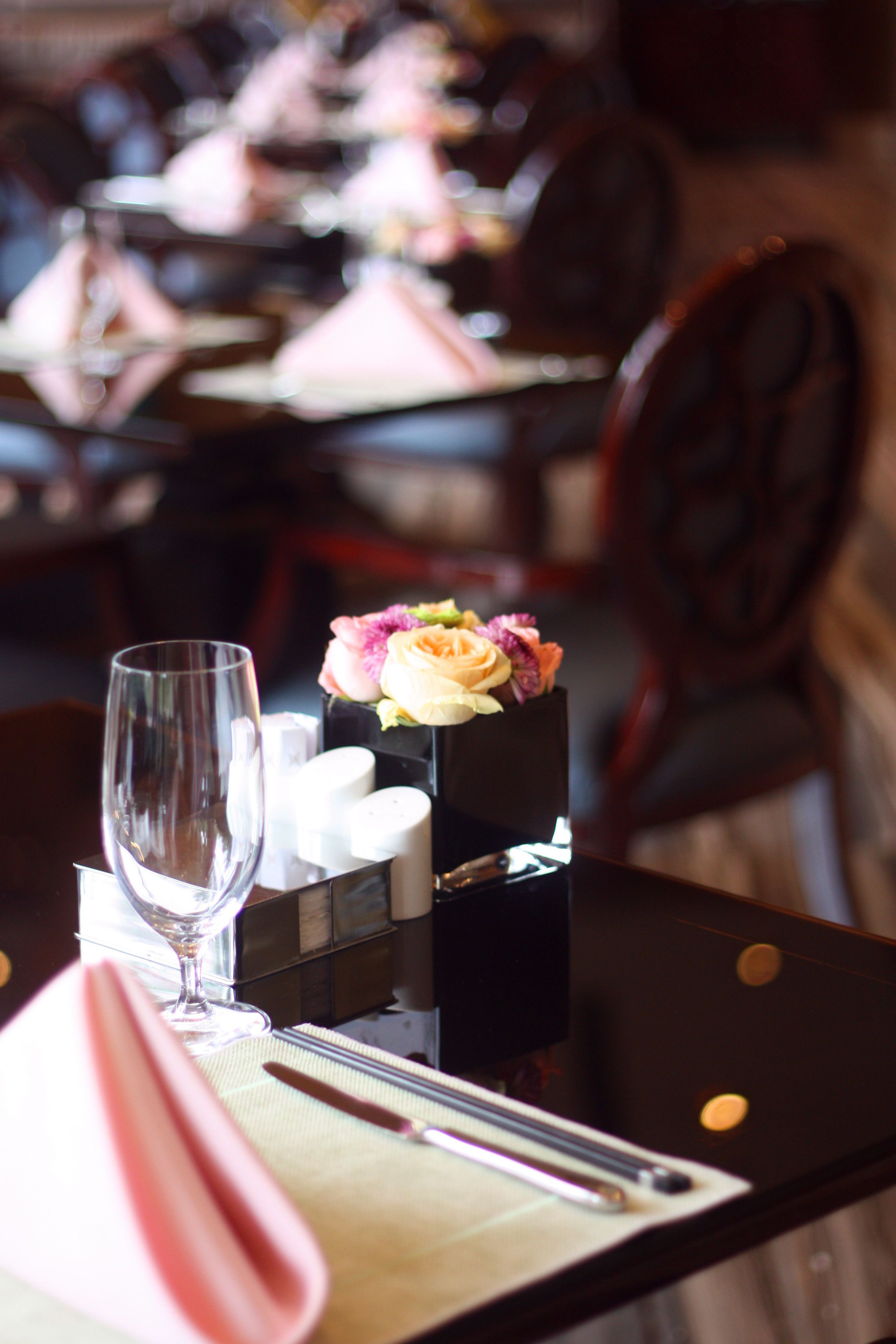 A dining table with a glass, napkin, cutlery, and a small vase with flowers.