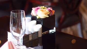 A dining table with a glass, napkin, cutlery, and a small vase with flowers.