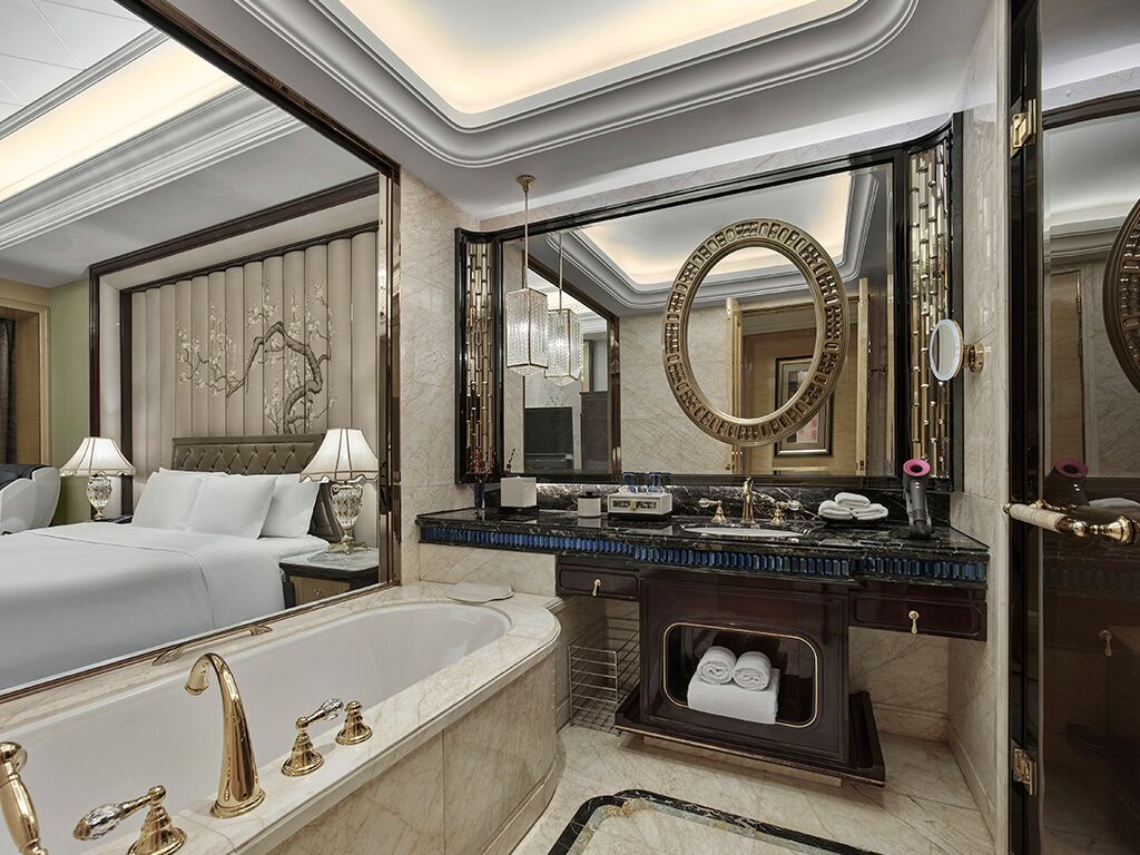A luxurious bathroom with a large bathtub, a vanity with a mirror, and a bed in the adjacent room.