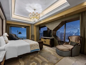 A hotel room with a bed, a TV, a desk, a chair, and a view of a cityscape.