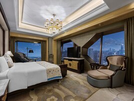 Habitación de hotel con cama, televisión, escritorio, silla y vista a un paisaje urbano.