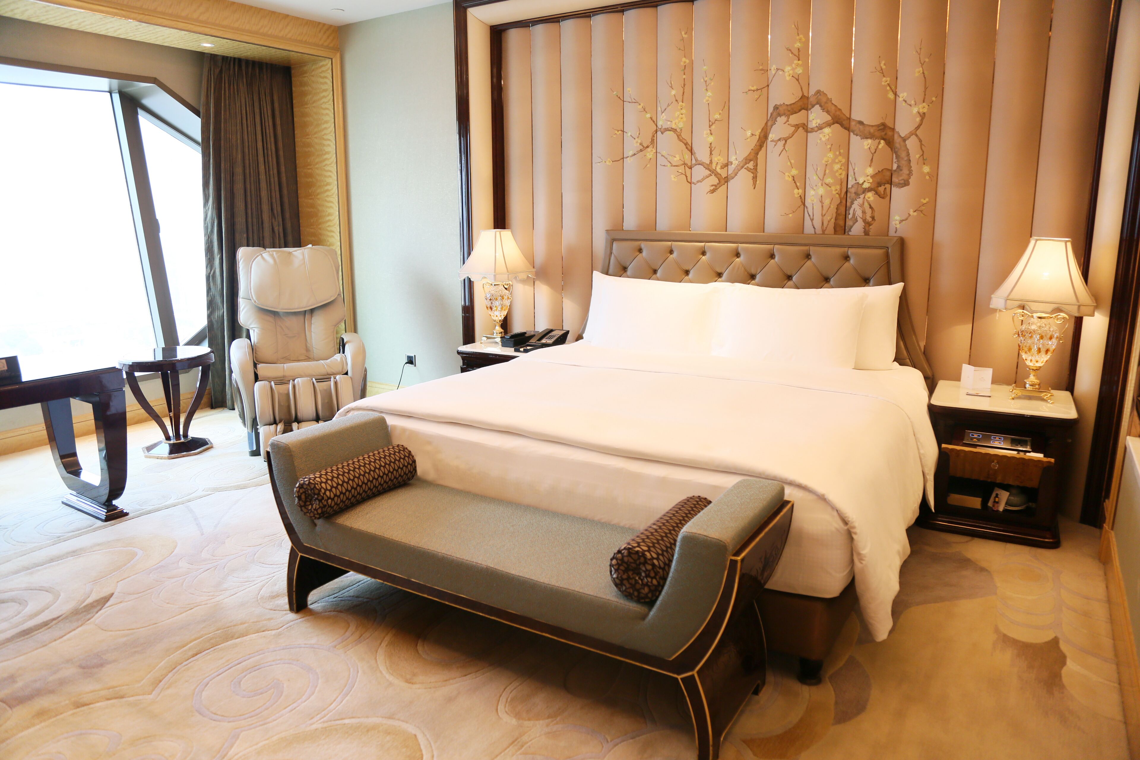 A hotel room with a large bed, a bench, a desk, and a chair.