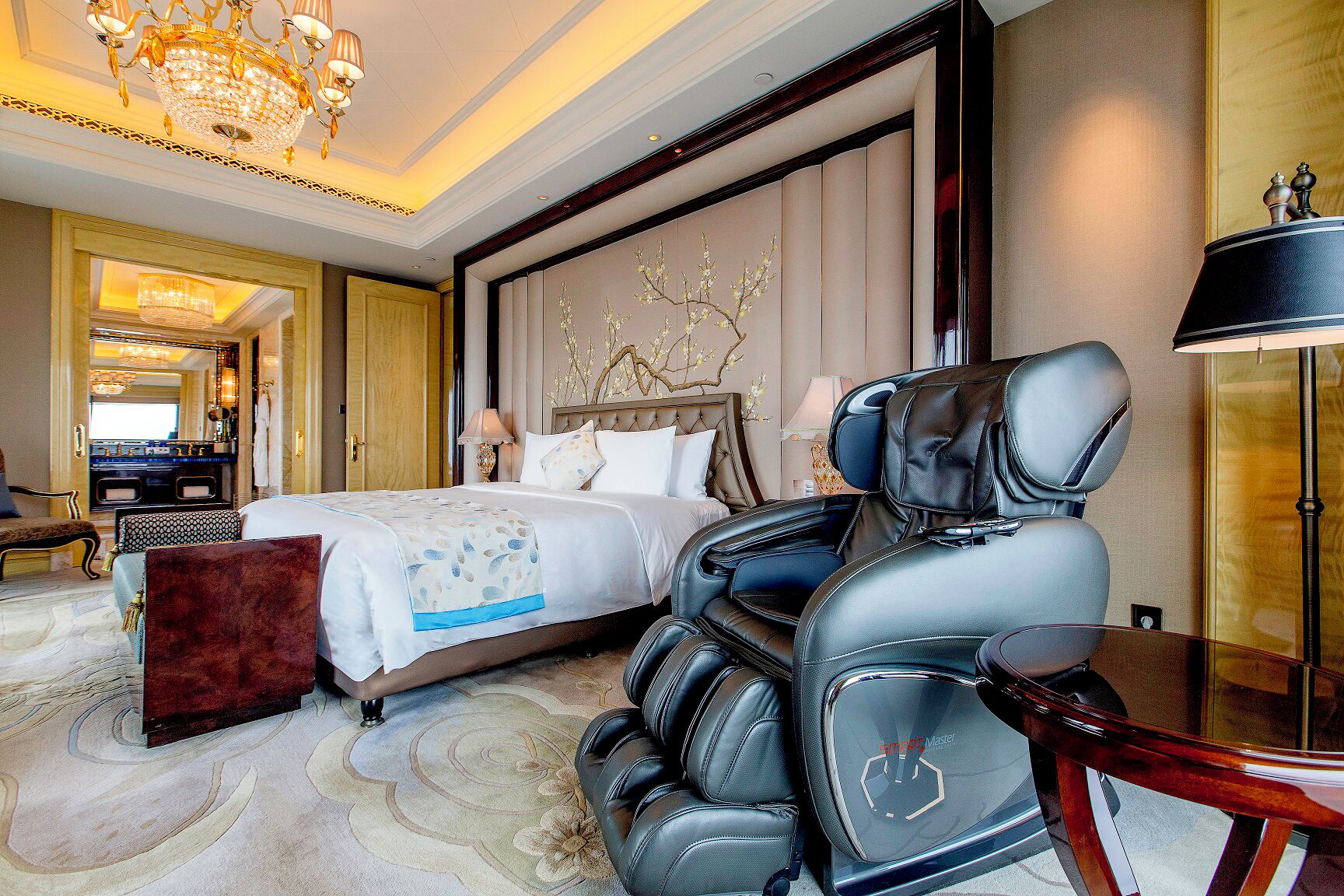 A hotel room with a bed, massage chair, and a large mirror.