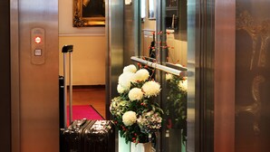 Um elevador com uma mala preta, um tapete vermelho e uma composição floral branca.