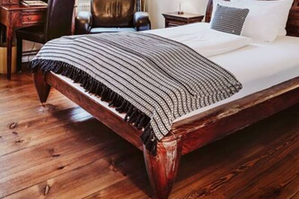 A classic room with a large bed, a desk, a chair, and a painting on the wall.