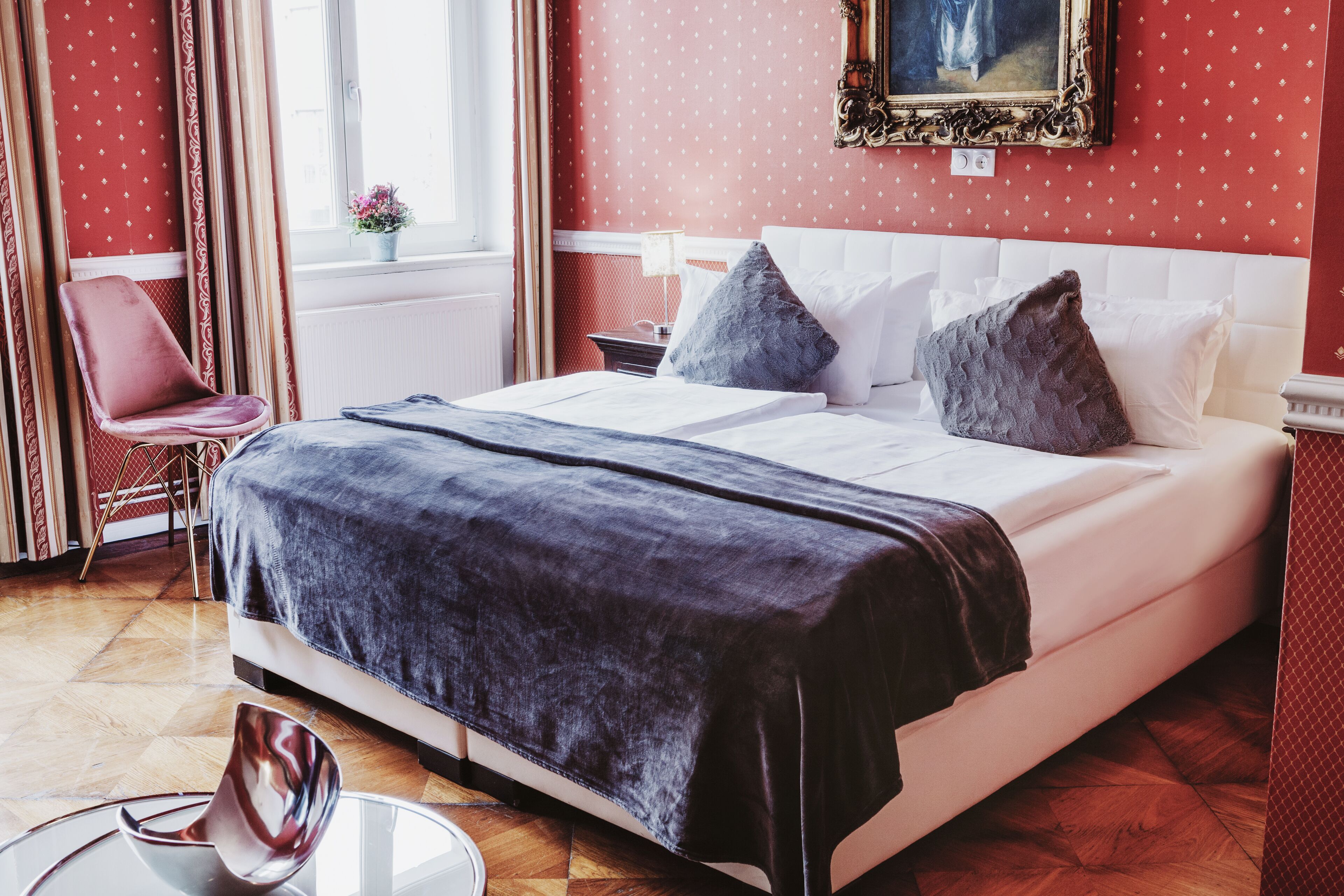 A hotel room with a bed, a chair, a table, and a window with curtains.