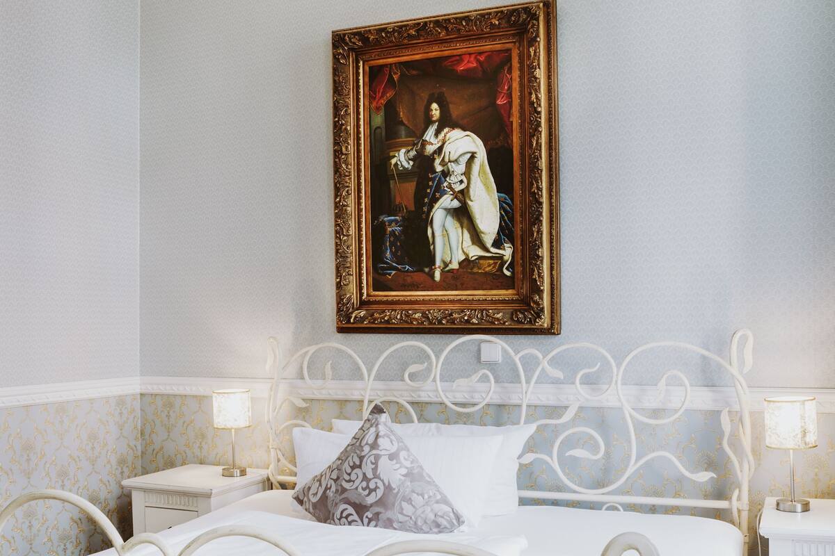 A bedroom with a bed, nightstands, a framed painting, and a patterned wall.