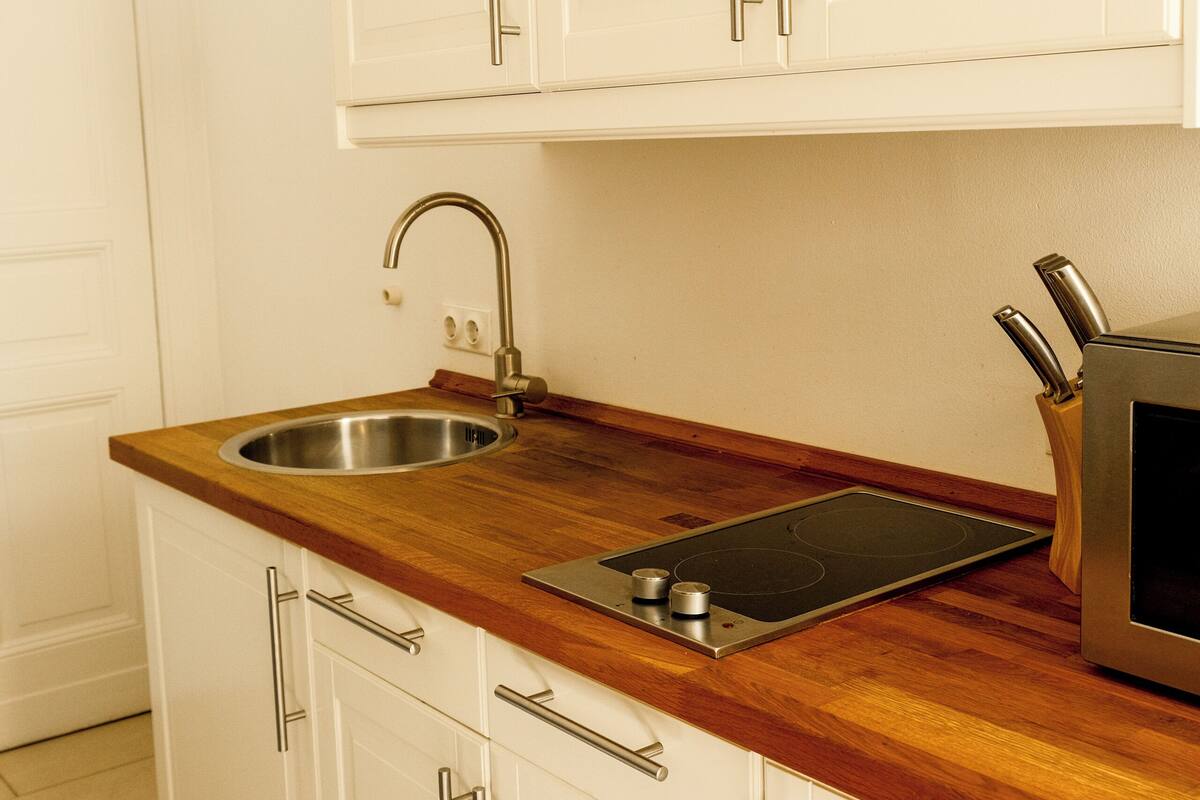 A kitchen with white cabinets, a stainless steel sink, a wooden countertop, and a built-in oven.