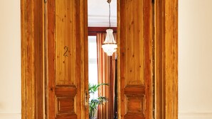 Uma porta dupla de madeira com o número "2" que dá para um corredor com um candelabro e um vaso de planta.