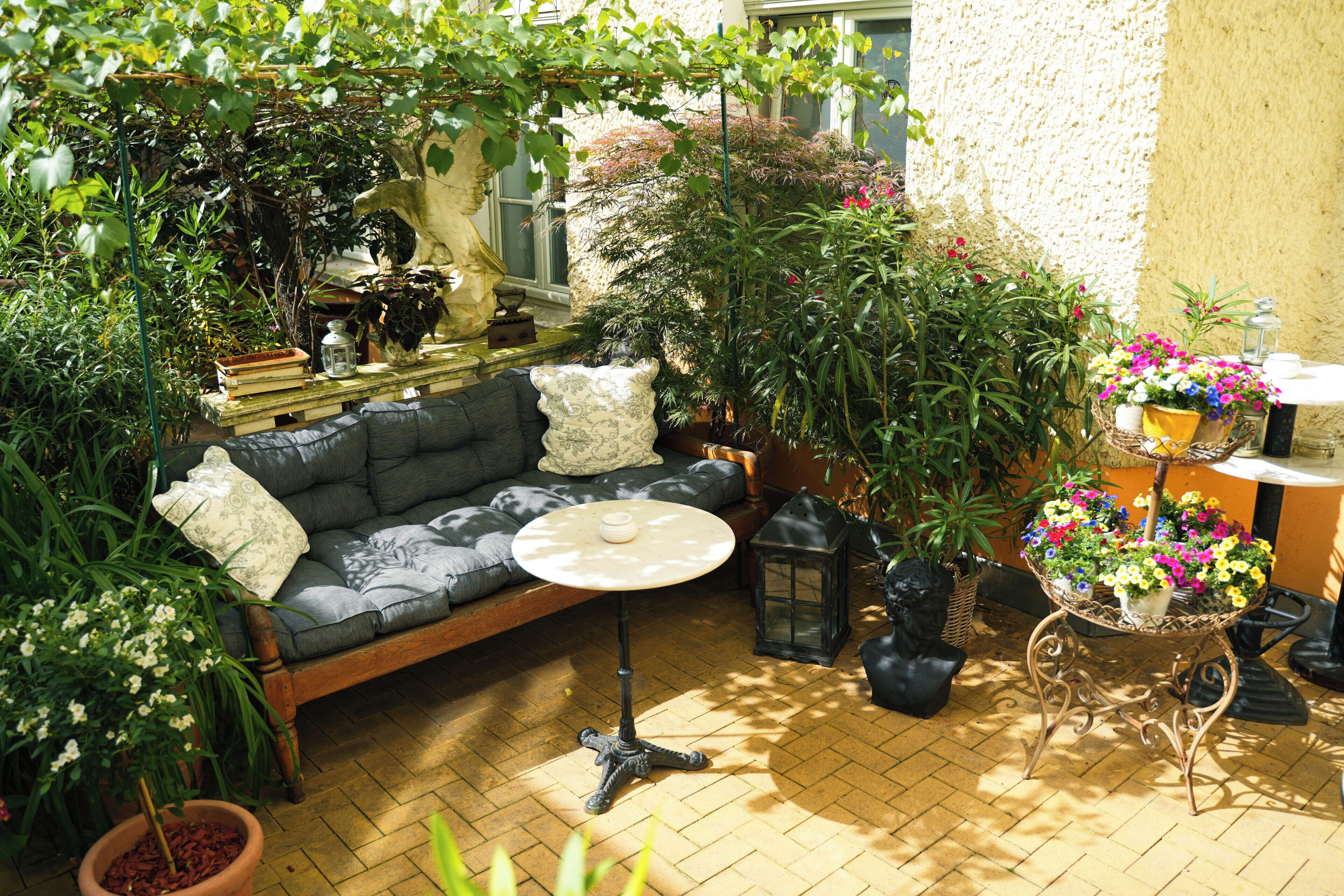 A cozy outdoor seating area with a sofa, a small round table, and various potted plants.