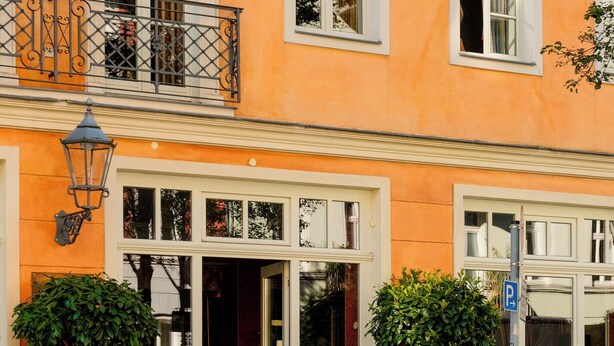 Um edifício com fachada laranja vibrante, janelas amplas e uma varanda com grade de ferro forjado.