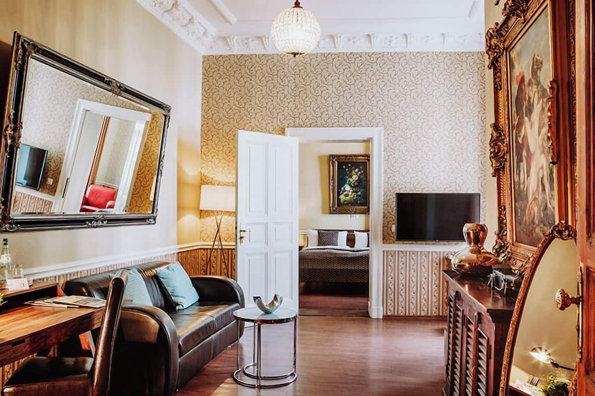 A room with a sofa, a small round table, a TV, a chandelier, and a large mirror.