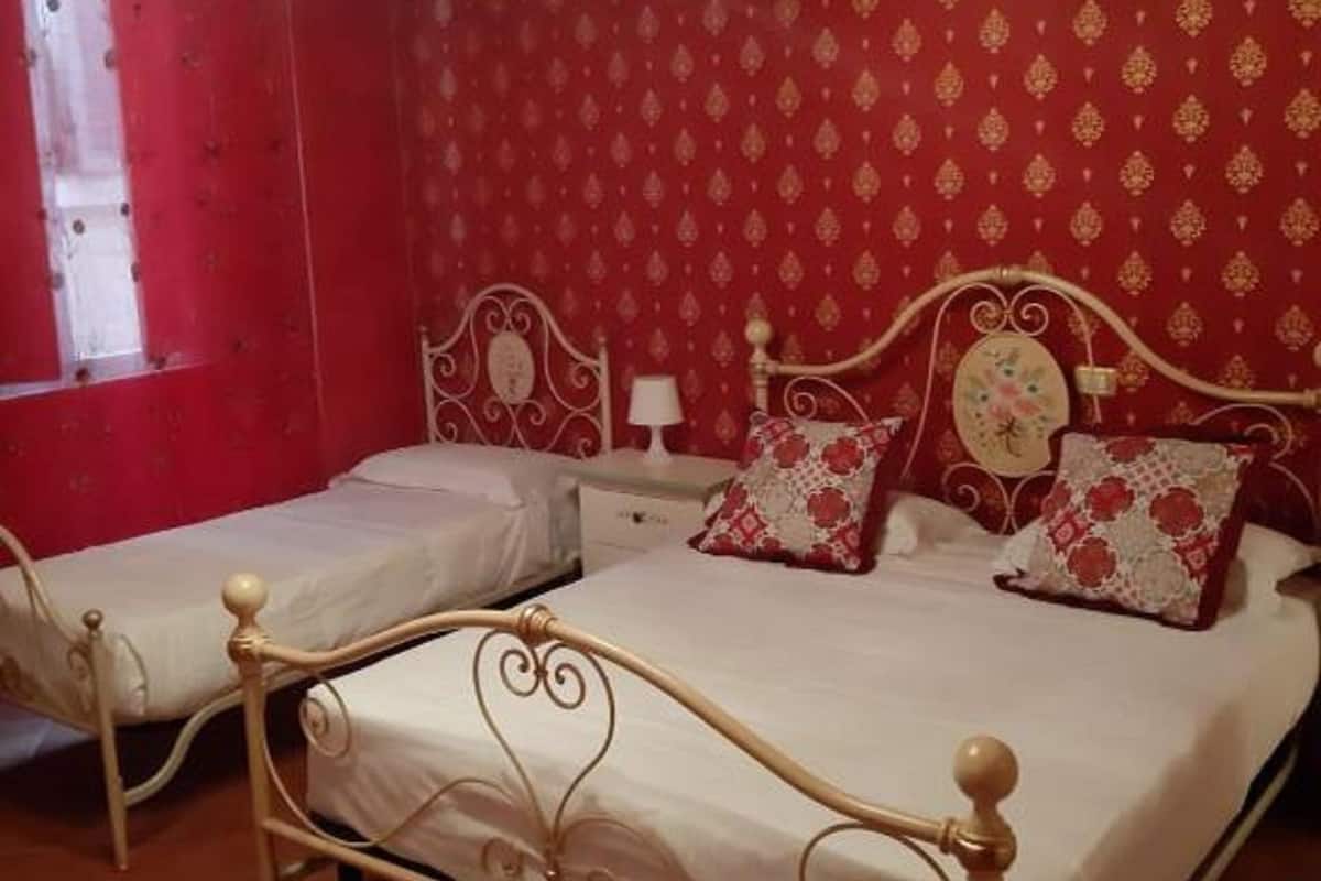 A bedroom with two single beds and a larger double bed, all with ornate metal frames.