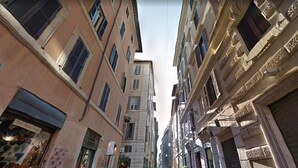 A narrow street with tall buildings, some with visible shop signs. - Nova Domizia (Rome)