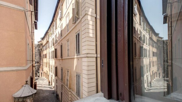 A narrow street with buildings on either side, a visible window frame, and a small lamp post. - Nova Domizia (Rome)