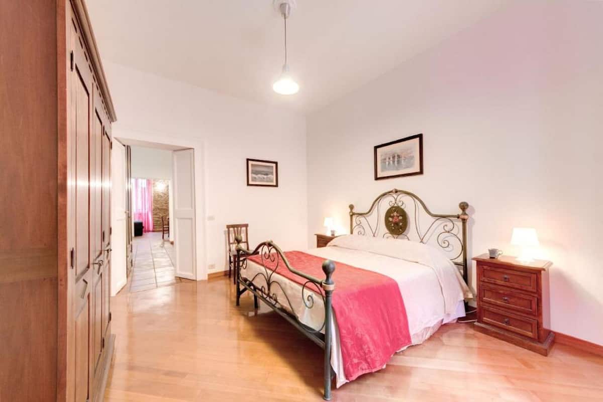 A bedroom with a bed, wooden wardrobe, bedside table, and a framed picture on the wall.