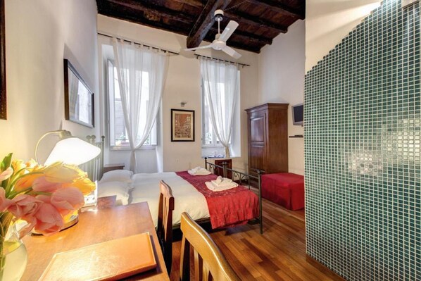Una habitación de hotel con techo de madera, cama con una manta roja, una mesa de madera con un jarrón de flores y pared con azulejos verdes.