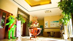 A hotel lobby with a reception desk, a large decorative vase, and a mascot.