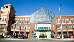 A hotel with a modern glass facade, a prominent entrance, and a parking lot with several cars.