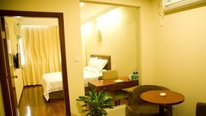 A hotel room with a bed, a desk, a chair, a potted plant, and an air conditioning unit.