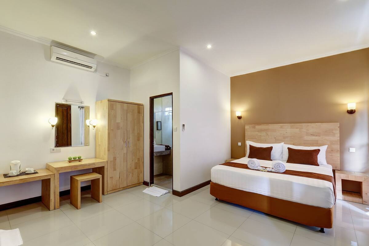 A modern hotel room with a wooden desk, a bed with brown bedding, and a bathroom visible through an open door.