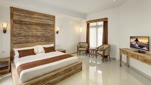 A modern bedroom with a large bed, a wooden headboard, a TV, two chairs, and a small table. - Nipuri Hotel (Keroboken Kelod)
