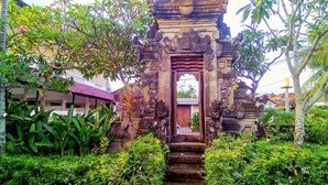 A traditional stone gateway with steps leading to a door, surrounded by lush greenery and a building in the background. - Nipuri Hotel (Keroboken Kelod)