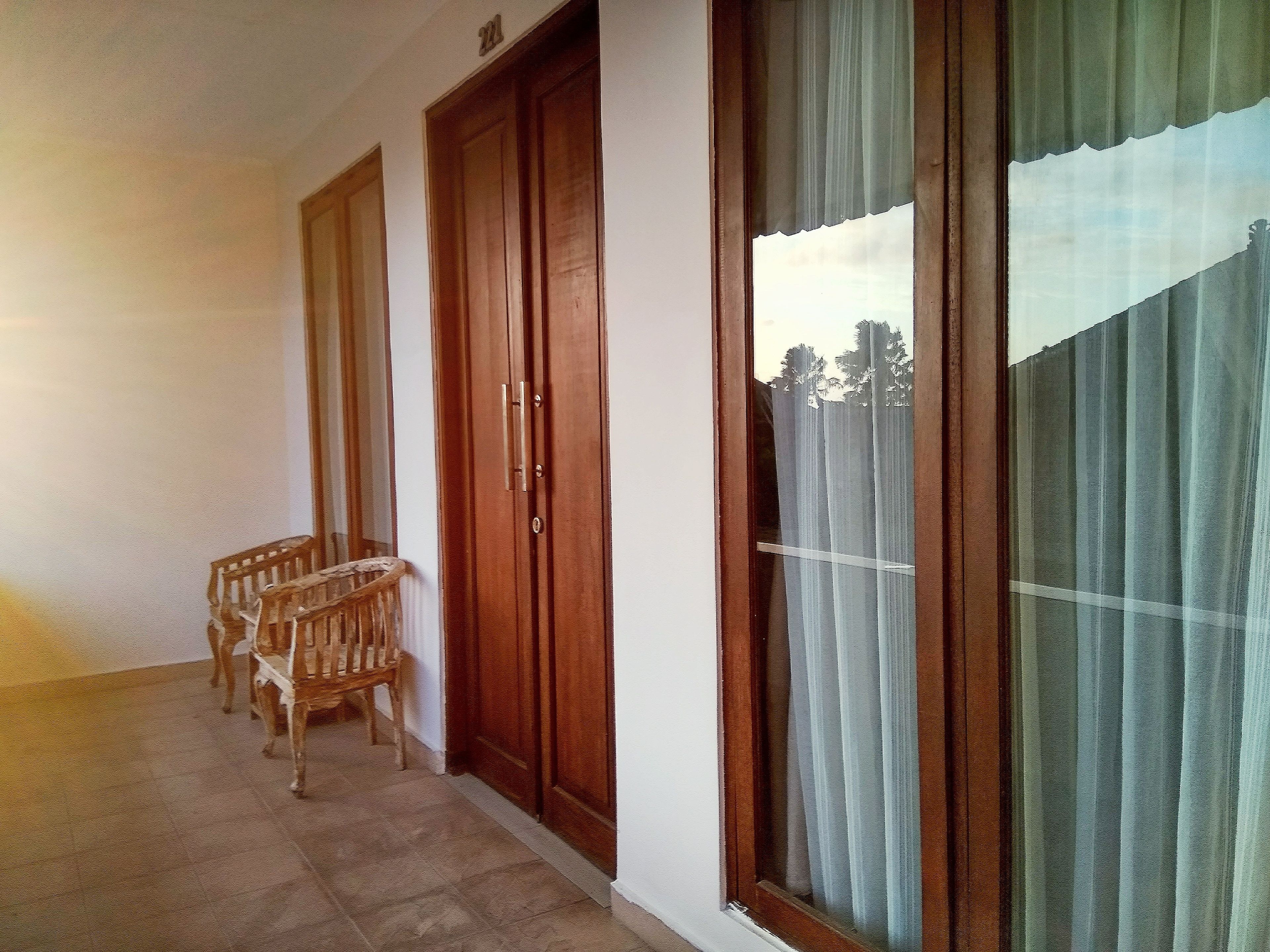 A hallway with a wooden door, a window with curtains, and a wicker chair.