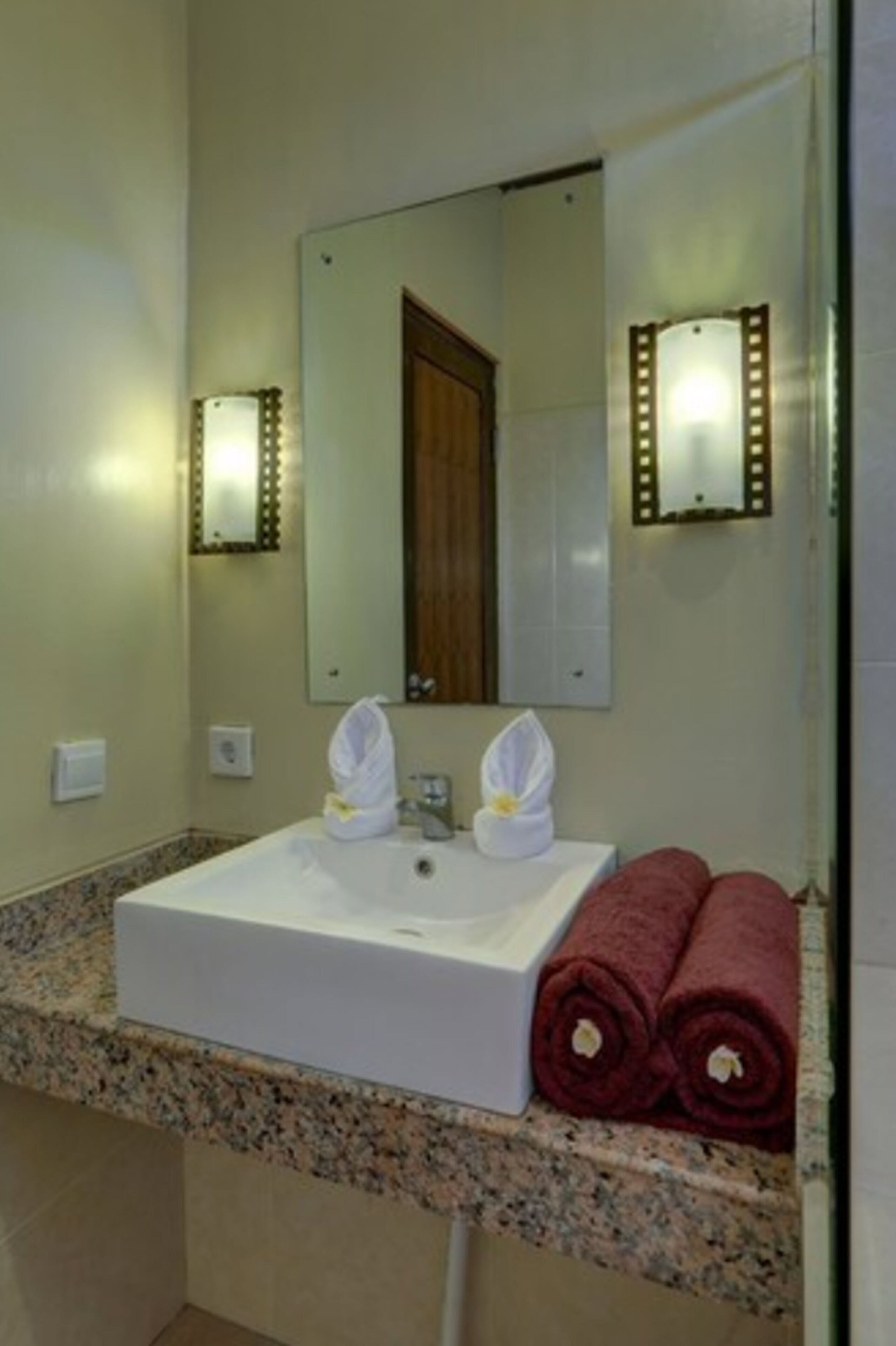 A bathroom with a white sink, two white towels, and a mirror with lights.