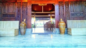 A traditional wooden structure with intricate carvings and two large vases at the entrance. - Nipuri Hotel (Keroboken Kelod)