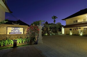Hall de hotel bem iluminado, com placa, entrada de automóveis pavimentada e jardim ajardinado.