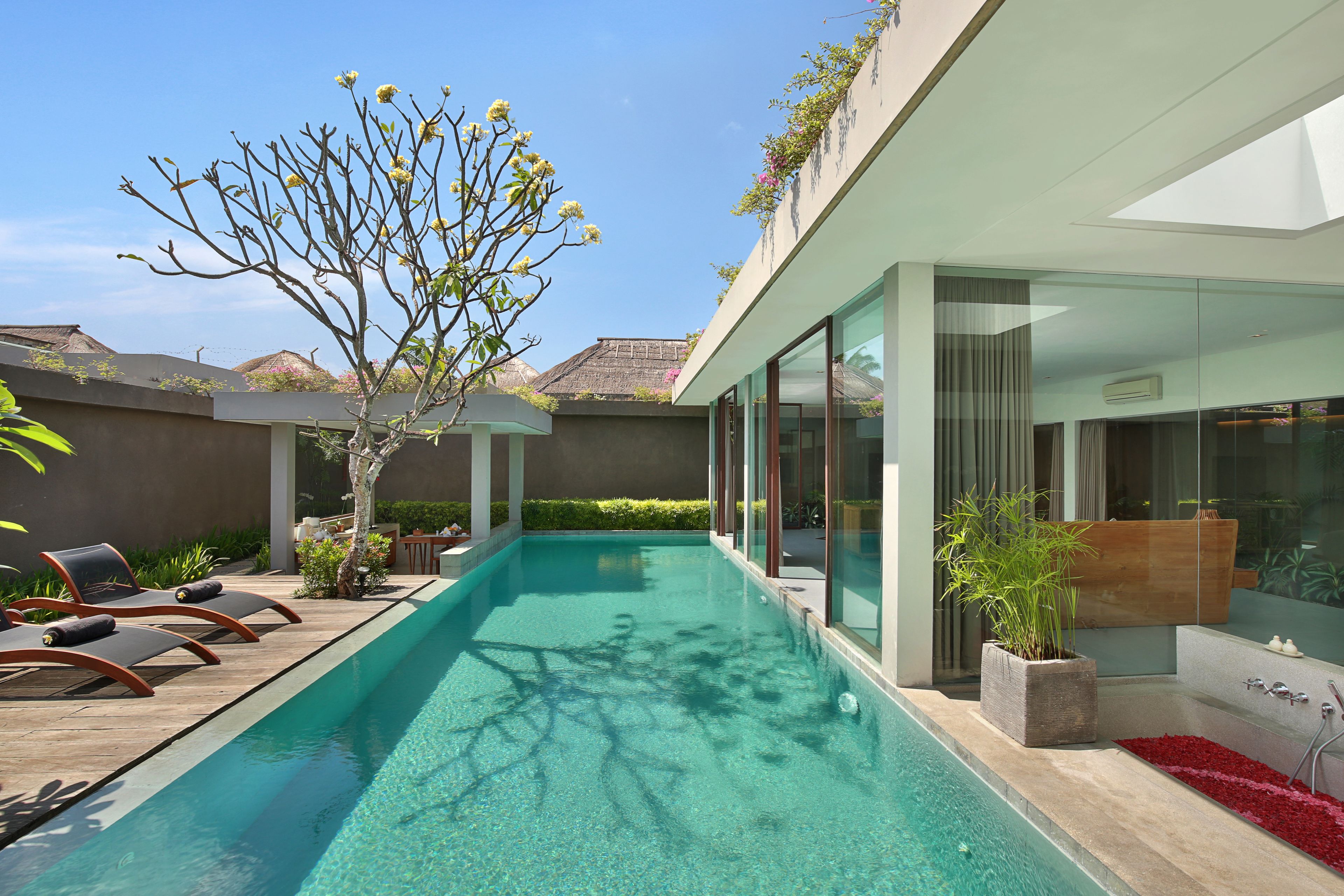 A modern pool area with lounge chairs, a clear pool, and a glass-enclosed spa area.