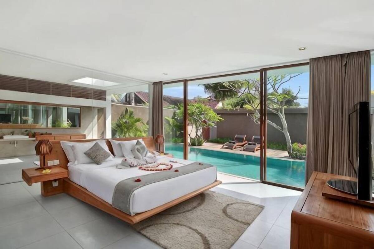 A modern bedroom with a large bed, a TV, and a view of a swimming pool.