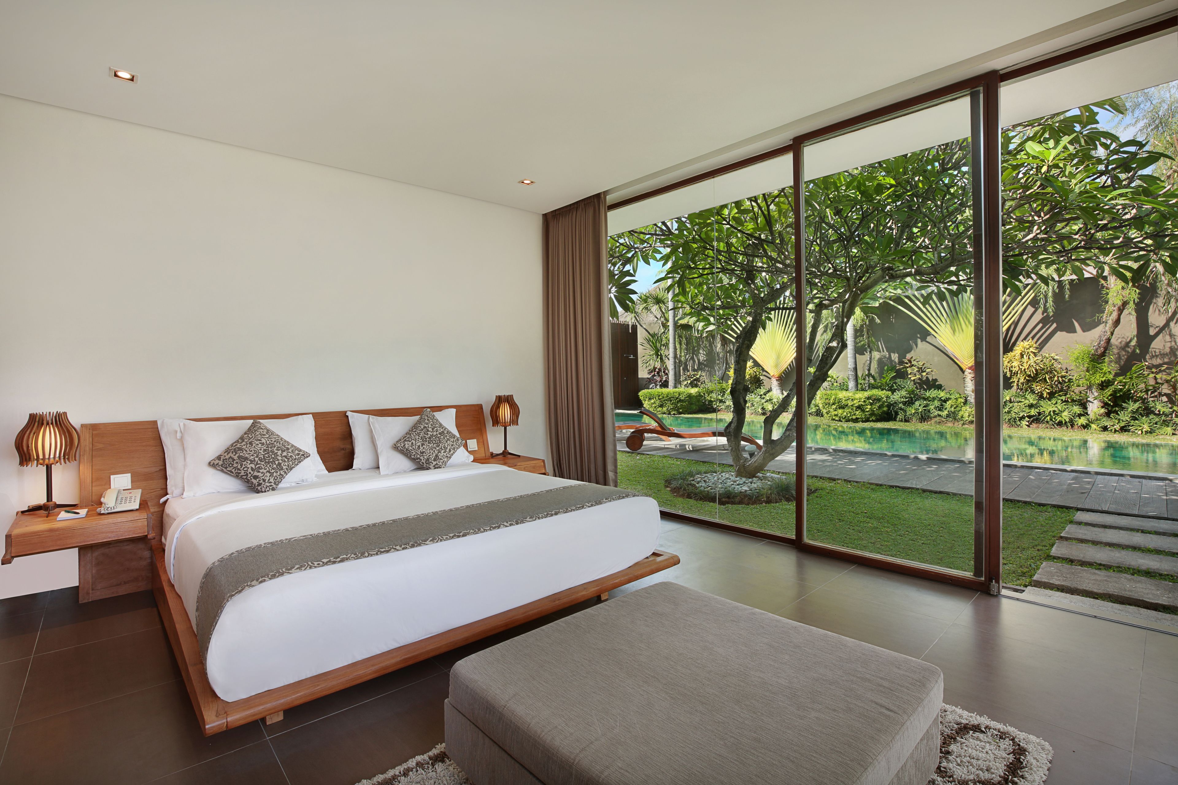 A modern bedroom with a large bed, bedside tables, and a view of a swimming pool and garden.
