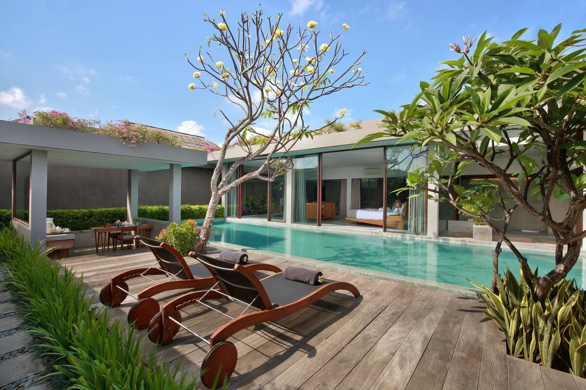 A modern outdoor pool area with wooden loungers and a glass-enclosed living space.
