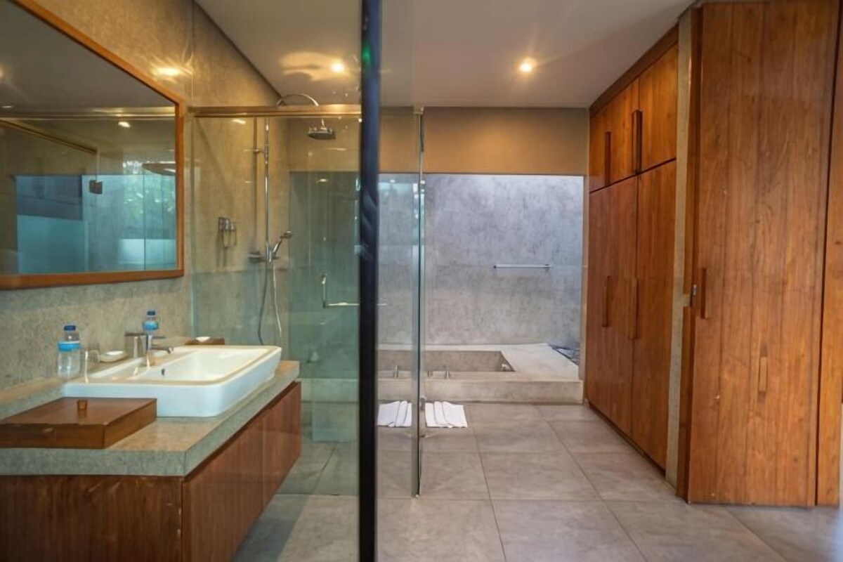 A modern bathroom with a glass-enclosed shower, a large mirror, a wooden cabinet, and a bathtub.